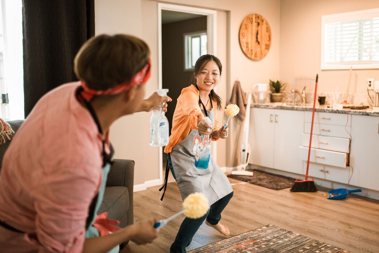 Un couple asiatique s’amuse en nettoyant leur maison, créant une ambiance joyeuse.